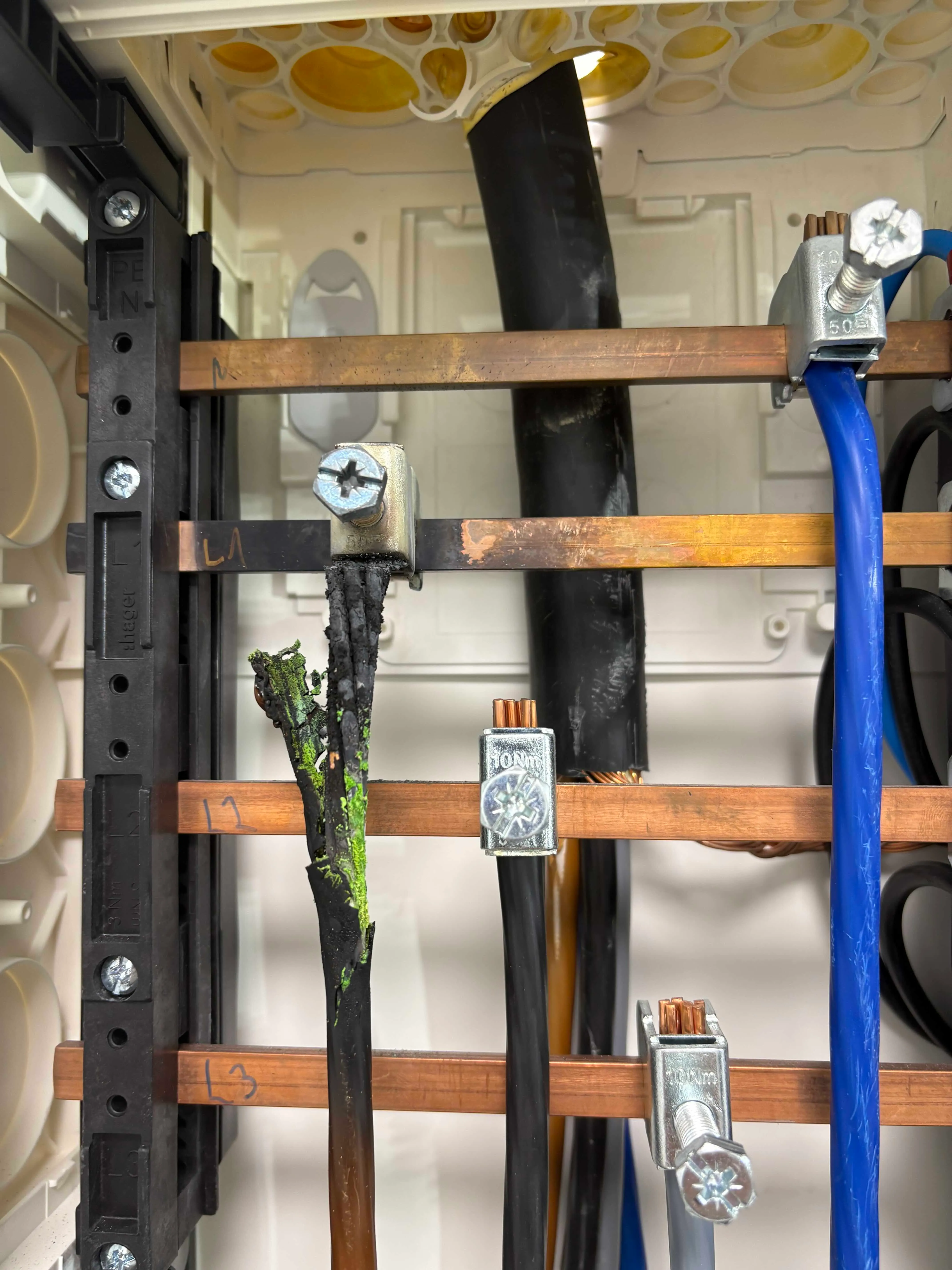 Verkohlte Aderisolation an einer lockeren Sammelschienen-Klemme L1 mit grünlichen Schmelzspuren am Kupfer – Originalaufnahme aus einer Hauptverteilung.
